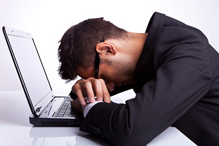 Man with head down in front of laptop. Panic attacks can feel very scary. Learn CBT tools to cope with anxiety and panic. 