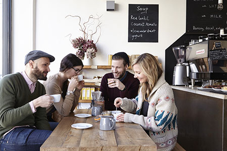 Four friends sitting and smiling in coffee shop while talking. Use CBT therapy to beat social anxiety.