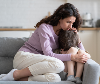 Worried mother hugs her anxious child while sitting on a sofa. Learn to respond to children with anxiety and OCD using SPACE Therapy. 